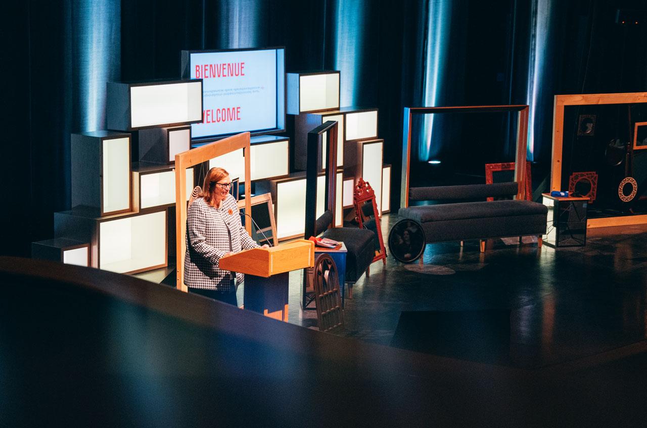 Marsha Walden prend la parole devant un décor composé d’objets rectangulaires et d’une enseigne de bienvenue.