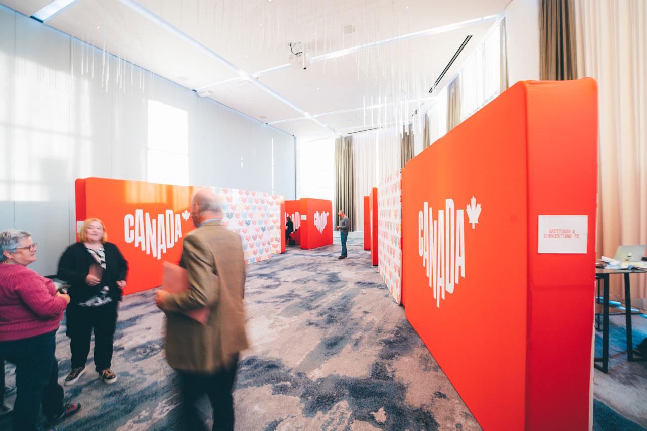 Des gens se tiennent près d’un mur décoré du logo Canada en forme de cœur.