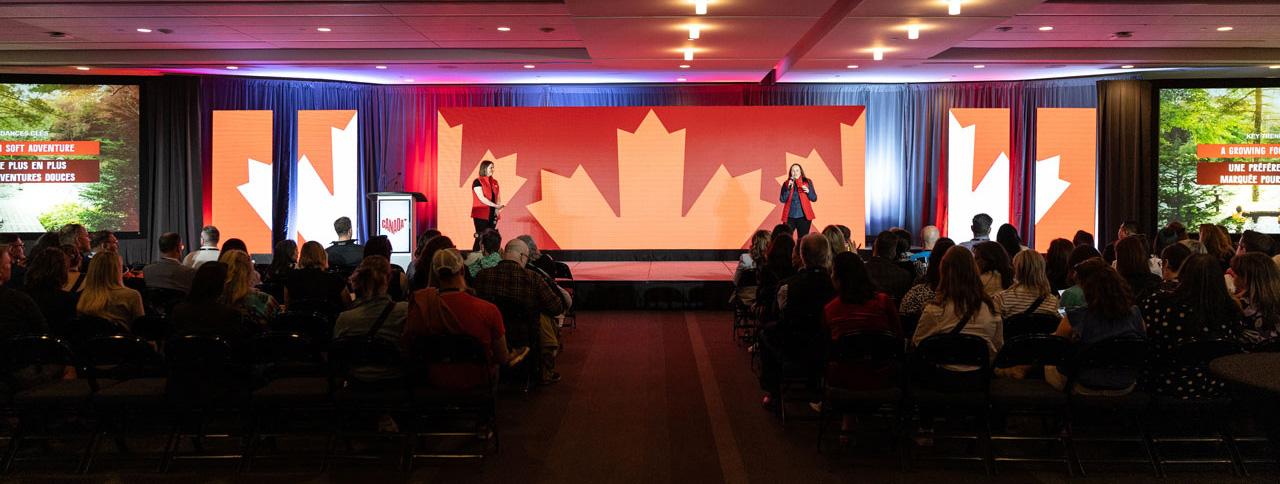 Wide angle of a presenters on stage with a maple leaf design backdrop